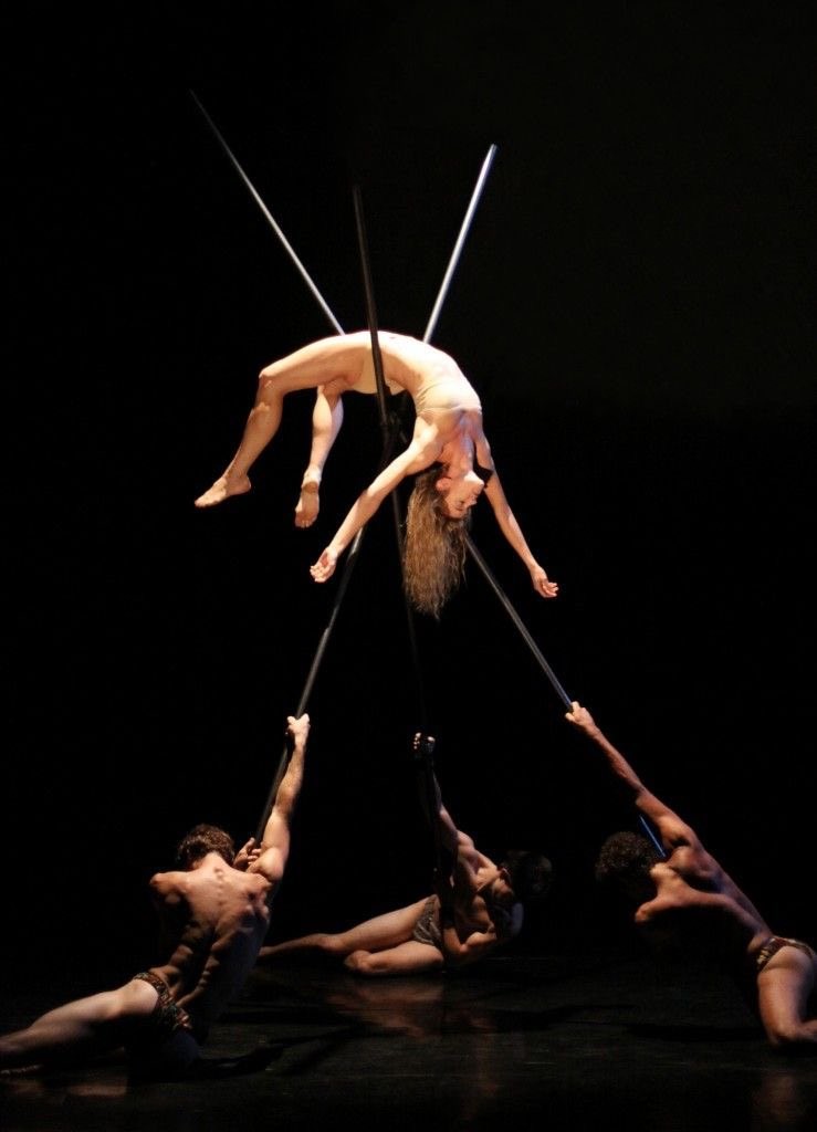 three men hold up a woman with three criss crossed poles she lies on