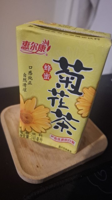 Caixinha de papelão (estilo toddynho), amarela e com o desenho de algum tipo de flor amarela. A caixa contém caracteres completamente indecifráveis, pois estão em chinês.