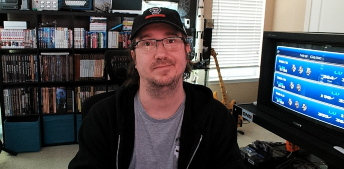 A picture of me sitting beside the AV cart showing FF6 playing on a flashcart.  The background shows a bookshelf full of nerdery and general geekery.
