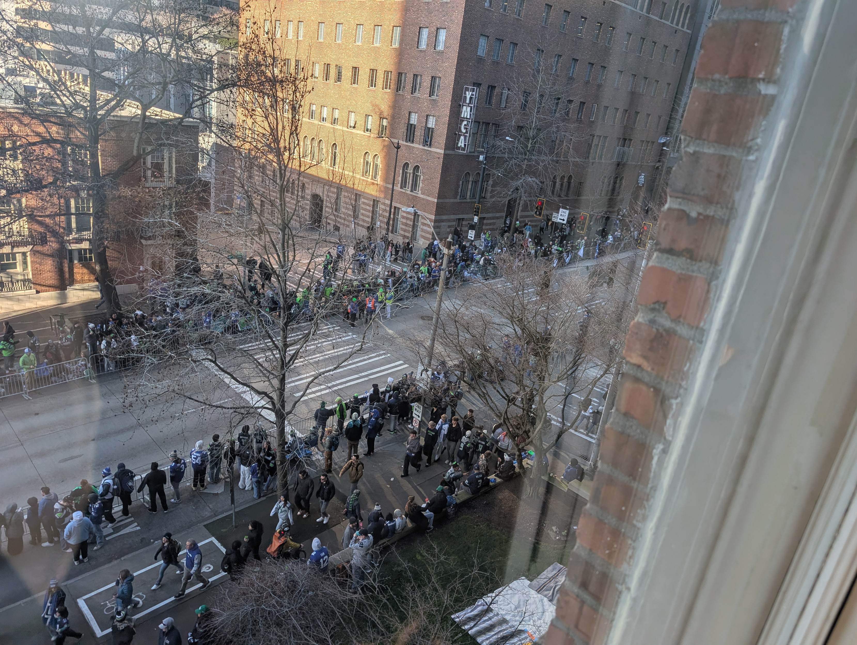 A bunch of sportsball fans on the sidewalk waiting for their favorite characters to go by.