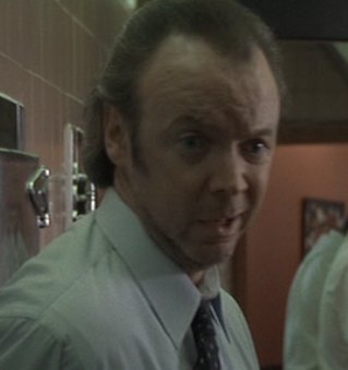 Filmstill aus 'Heat' (1995) von Michael Mann: Bud Cort als Solenko, der schmierige Imbissbudenmanager. Unrasiert, mit zynischem Gesichtsausdruck, die rechte Augenbraue verächtlich hochgezogen, die Haare mit weit zurückweichendem Haaransatz glatt nach hintengekämmt. Eine durch und durch unsympathische Rolle.