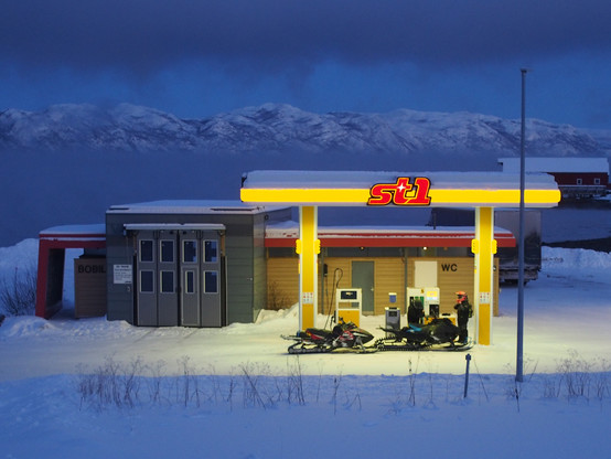Photo of two snow mobiles refuelling at a ST1 petrol station, with snowy mountains in the background