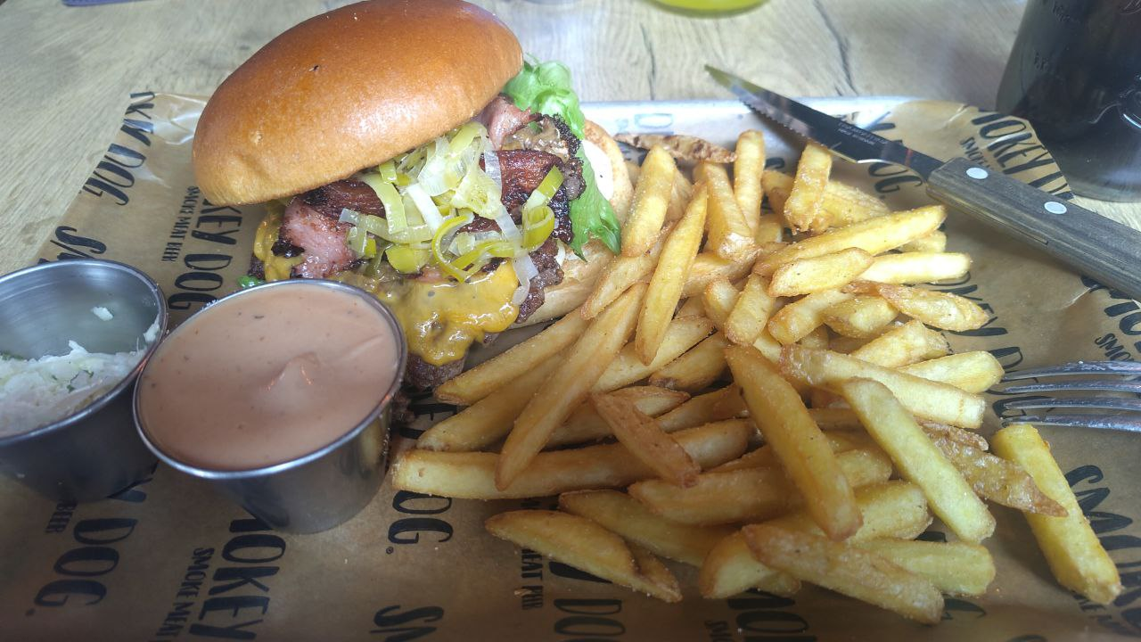 överfull burgare som är påväg att välta och en hög med pommes runt den.
liten skål i rostfritt med chipottelmajo och en likadan skål med coldslaw