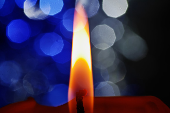 Nahaufnahme einer Kerzenflamme (orange), Hintergrund sind blaue und weiße Blendenflecken (bokeh)