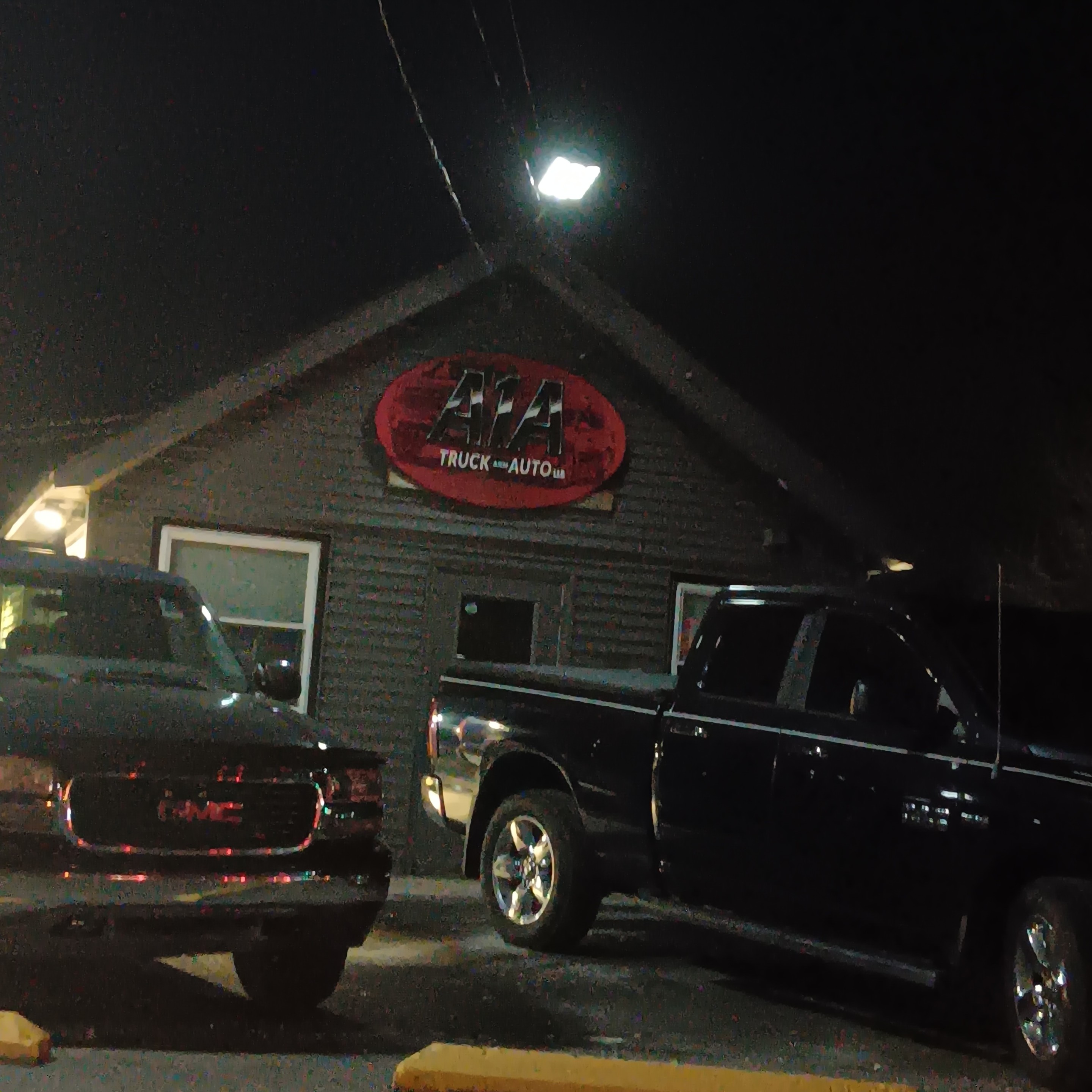 two black trucks parked in front of the little building at night
