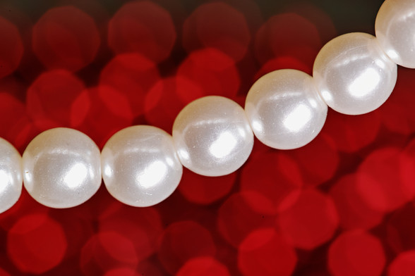 Nahaufnahme einiger Kunst-Perlen einer Halskette. Im Hintergrund rote Bokeh-Bubbles.