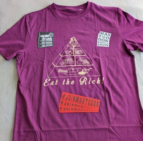 Beerenfarbiges T-Shirt. 

Aufdruck in Gold: Lebensmittelpyramide, mit einer Figur ähnlich dem Monopoly Männchen an der Spitze.
Darunter die Aufschrift "Eat the Rich!"

Auf dem T-Shirt liegen je drei Stück drei verschiedener Aufkleber.