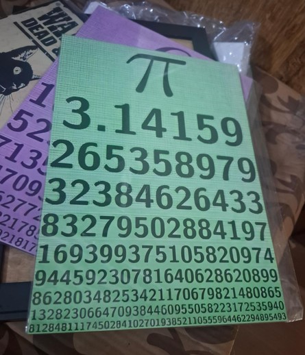 Um pequeno quadro de madeira, sem moldura, em que vemos o símbolo de pi seguido por seu valor com precisão de mais de cem dígitos após a vírgula.