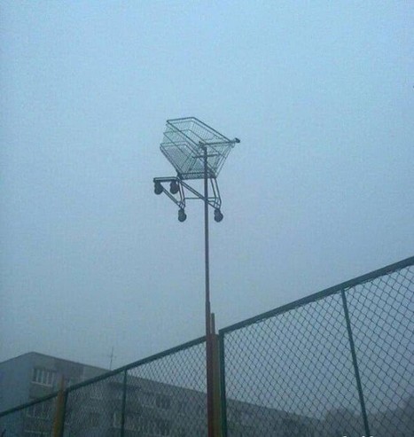SHOPPING CART CRUCIFIED HANGING FROM POLE UNDER DULL BLUE SKY