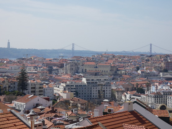 Vista panorámica de Lisboa, sus tejados y el puente colgante. Se ve también una estatua de una T enorme.