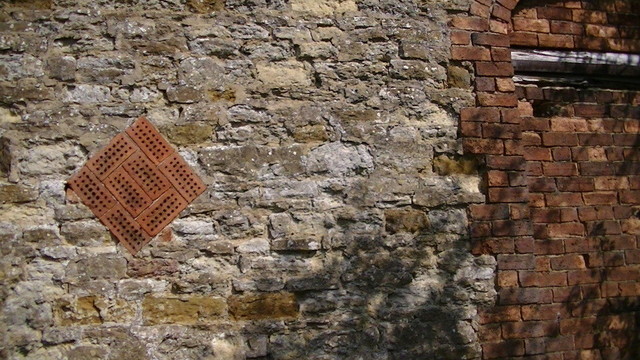 a diamond configuration made up of 8 holed red bricks on their side, in a stone wall. view from the outside. idk what this type of brick is called. the square holes go through the brick from the top to bottom.