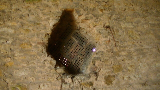a diamond configuration made up of 8 holed red bricks, on their side, in a stone wall. view from inside.