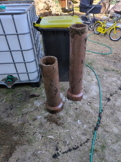 Im Vordergrund zwei Keramikröhren, ca 1m lang und 20cm Durchmesser, dahinter unter anderem eine gelbe Tonne und ein IBC Container