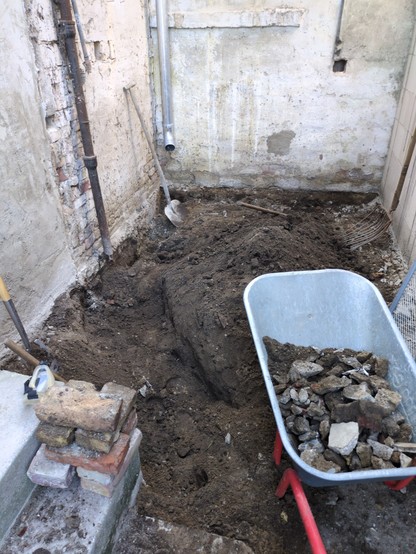 Frischer Erdaushub in einer Hausecke, Schubkarre mit Schutt