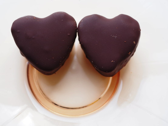 zwei Herzen mit Schoko-Überzug (der Inhalt ist Fruchteis) auf einem Glasteller. Die Herzen wirken wie Augen, der Glasteller wirkt wie ein lächelnder Mund.