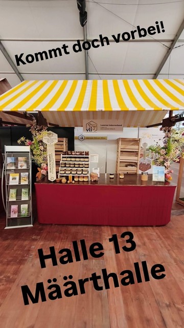 Ein Marktstand mit roter Theke und weiss gelbem Stofdach. Auf der Theke hat es verschiedene Bienenprodukte.