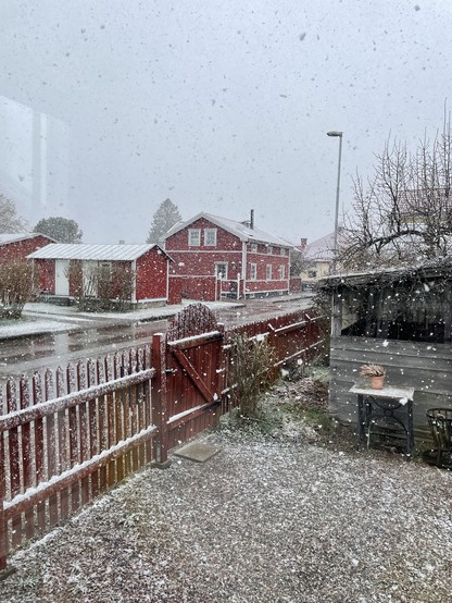 En bild knäppt genom ett fönster. Utanför faller stora snöflingor som ligger kvar på hustaken