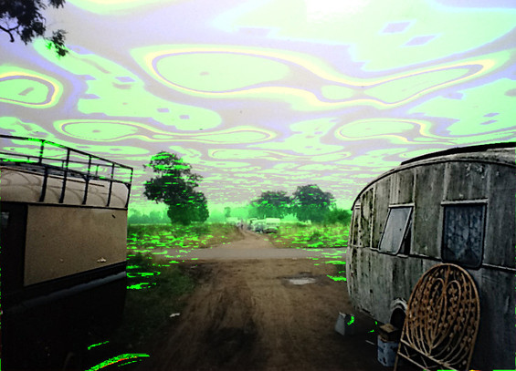 a photo of a traveling hippy site on a wide bridleway from the 1990s that i messed around with in GIMP about 7 years ago. landrover on the left, Cheltenham trailer on the right with a wooden headboard lent on it. swirly green paterns in the sky and ground. artifacts of distant vehicles, trees etc.