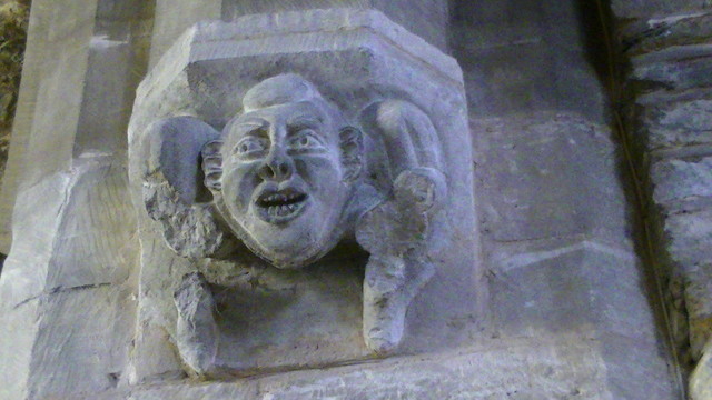 a medieval grotesque limestone face corbel at the bottom of an arch inside a church.
