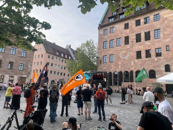 Kundgebung; vor einem Sandsteinhaus stehen Menschen auf einem Platz mit verschiedenen Fahnen, darunter die Fahne der Piratenpartei und einer vom Deutschen Hanfverband.