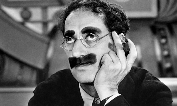 Una fotografía de Groucho Marx con su característico mostacho pintado, su cigarro habano y la mirada en el infinito.