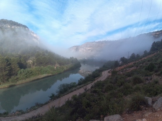En la foto se ve un meandro del río Júcar a la altura de la pedanía de Tolosa. Es un valle muu profundo con mucha vegetación a los dos lados. El río es bastante ancho. Hay un poco de niebla y se ve alguna casa del pueblo.