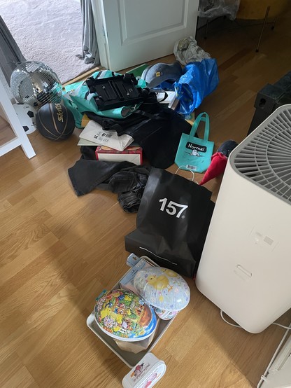 A cluttered indoor space with various items scattered on the floor, including a disco ball, basketball, bags, clothing, and decorative eggs.