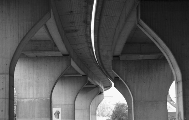Zwei Betonbrücken von unten betrachtet verlaufen in Form einer leichten S-Kurve fast parallel zueinander. Die Pfeiler wirken wie das Gewölbe in einer Kirche. Der Spalt zwischen den beiden Brücken ist schmal. Das Bild ist in schwarzweiß mit nur wenig Kontrasten.