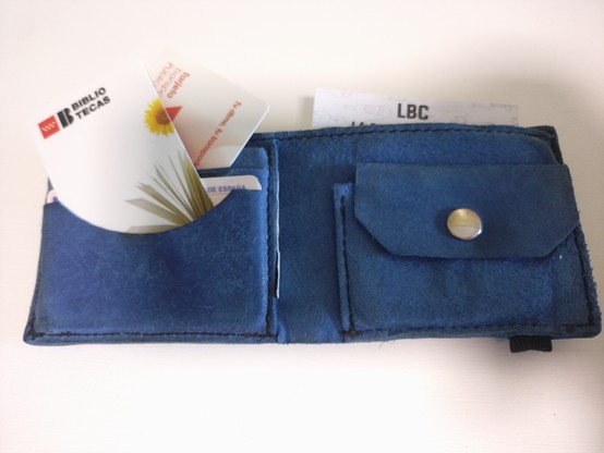 Se ve una cartera de piel azul de la que sobresalen un carnet de la red de bibliotecas públicas, una tarjeta de transporte público y la tarjeta de fidelización de una cervecería