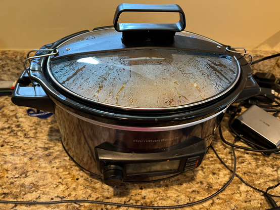 A slow cooker with about 4 hours left on the timer on top of a granite counter top.
