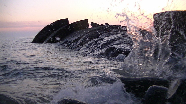 splashing wave against smooth grey sedimentary rocks just before sunrise. purple and pink sky.