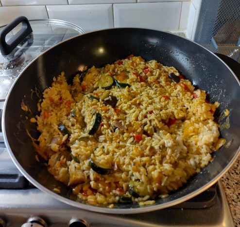 A wok containing a mix of yellowed rice and mediterranean vegetable bits. It looks slightly like it's melted together, thanks to the final ingredient, a generous splash of cream.