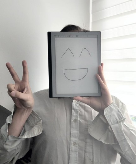 A person who has a PineNote instead of a face, doing a V-sign with his hand. He looks happy.