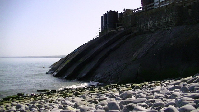 a factory on top of of folded layers of rock sticking out of the sea