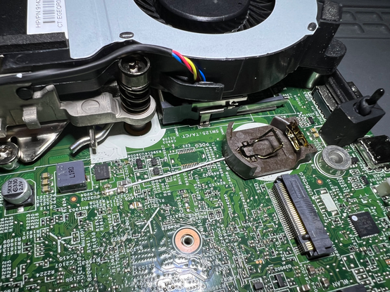 A picture of a computer motherboard with a new coin battery holder on it.  A bodge wire is run from underneath the holder to a convenient ground on the mainboard via a very smol white wire.