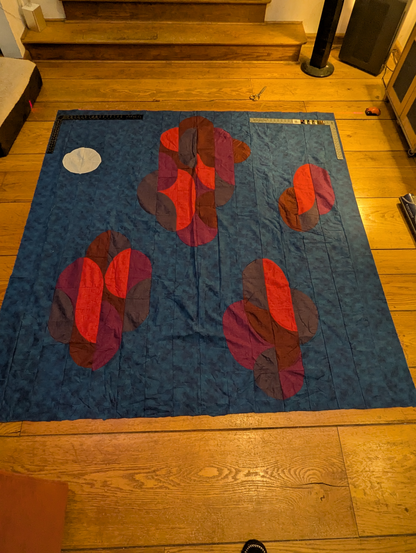 Quilt top layed on floor with two framing squares and a laser level on it.