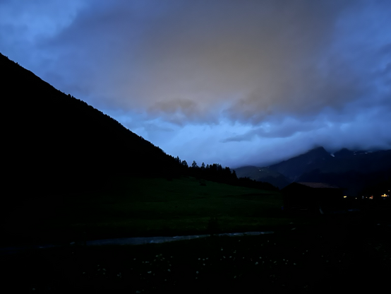 Dark mountainsides, clouds, blueish sky