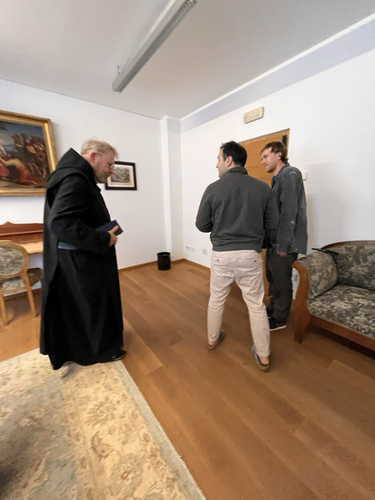 Benedictine monk in black robe and two other individuals 