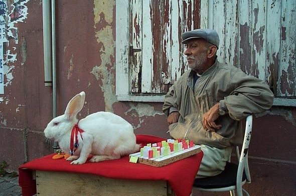 old turkish man with rabbit and table in front of chipped paint building