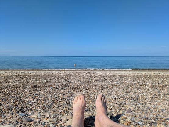 Foto fra Ellidsbøl Strand. Mine fødder i forgrunden, så strand og hav og BLÅ himmel.
Hvis du zoomer lidt ind kan du se min søde kone i vandet ☀️🏖️