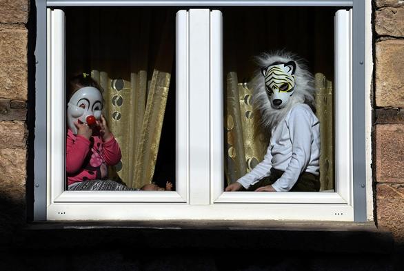Children wearing clown and tiger masks watch the carnival procession from a window of their house on the first day of the carnival celebration.