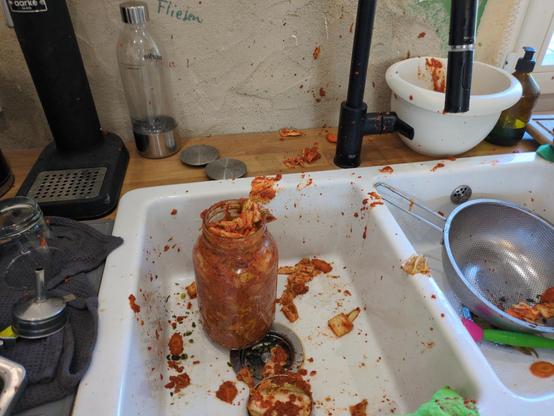 Offenes Kimchi Glas in einer Spüle.
Inhalt teilweise rundgerum und an den Wänden verteilt