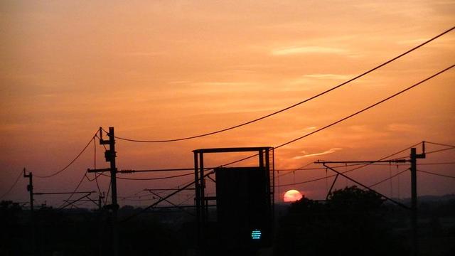 sunset behind railway overhead lines and green signal.