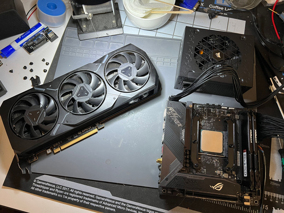 An AMD Radeon 7900XT GPU, a Corsair 1000W SFX PSU, and an ASUS STRIX X570-I Gaming motherboard sitting on top of a silicone pad.