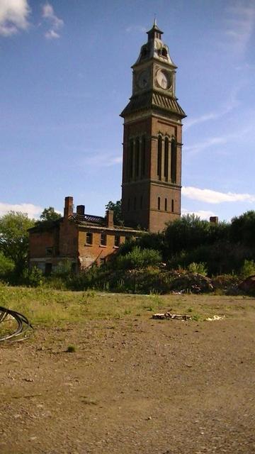 a derelict victorian clock tower next to a building with no windows or roof tiles on some wasteland