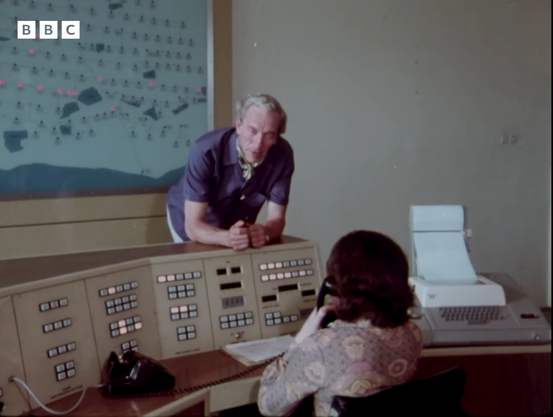 A huge control panel, a phone, two people, and a Teletype ASR-33