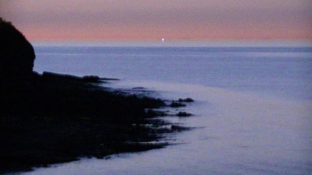 orange sky, blue sea, black silhouette of cliffs and outcrops into the sea. very grainy due to lack of light