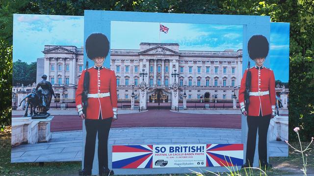 Ein Foto von einem Foto: zwei britische Gards vor einem Gebäude wo am Gibel die britische Flagge weht. Im Vordergrund ein Schild mit "So British!". Aufgenommen beim Fotofestival LaGacilly Baden.