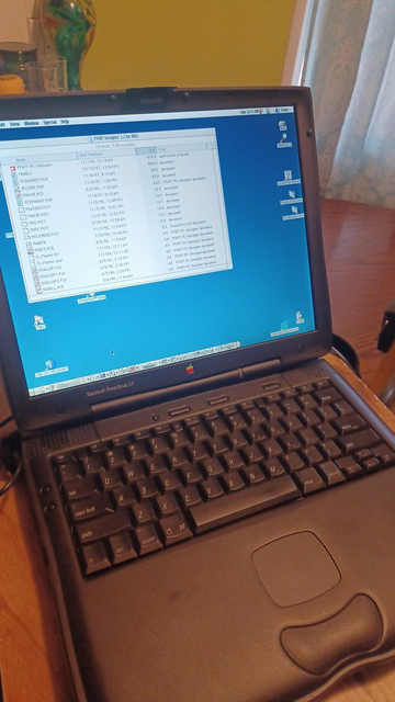 A black laptop sits on a counter, opened up. The screen is on and there is a program window open, with some icons on the desktop around it. It is an old laptop, with full desktop style keys in the keyboard.