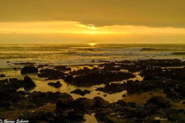 View of the ocean from Moonstone Beach, looking across rocks and gentle waves towards the setting sun.